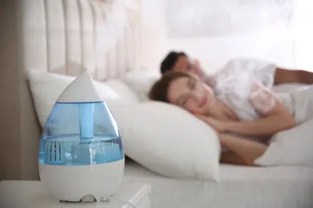 Un couple dort dans son lit à proximité d'un humidificateur d'air de couleur bleu allumé