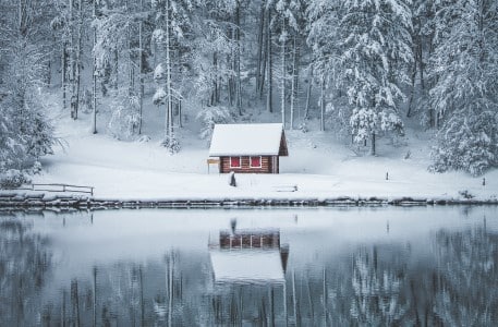 Chalet enneigé en lisière de forêt au bord d'un lac en hiver