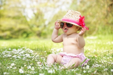 Bébé fille avec un chapeau et des lunettes roses assis dans l'herbe en pleine chaleur estivale