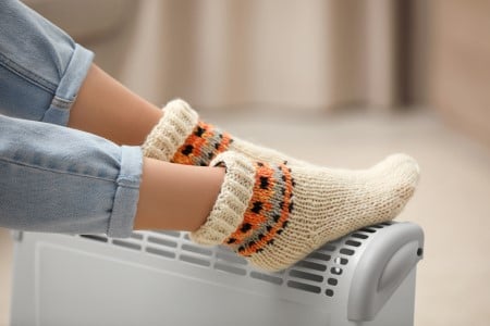 Femme qui se réchauffe les pieds sur un chauffage d'appoint électrique