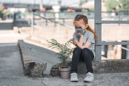 Enfant avec un masque de protection contre la pollution de l'air, regardant une plante verte en pot dans la rue