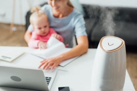 Humidificateur d'air allumé sur le bureau d'une femme télétravaillant avec son bébé sur les genoux
