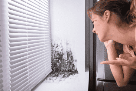 Femme choquée en découvrant de la moisissures dans l'angle d'une fenêtre