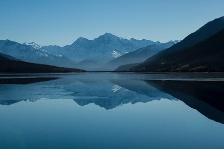 Reflet d'une montagne enneigé dans l'eau d'un lac sur fond de ciel bleu