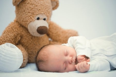 Bébé qui dort dans son lit avec un ours en peluche veillant sur lui