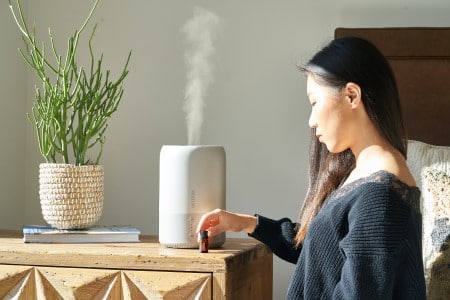 Femme asiatique assise dans sa chambre à côté d'un humidificateur d'air allumé prenant un flacon d'huiles essentielles