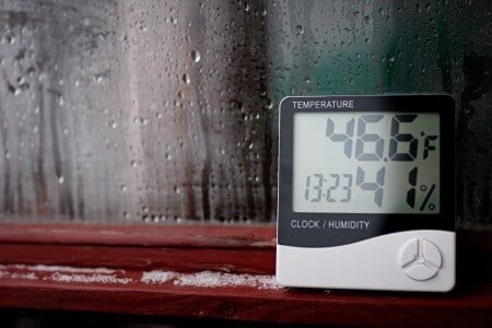 Thermomètre hygromètre posé contre une vitre recouverte de buée