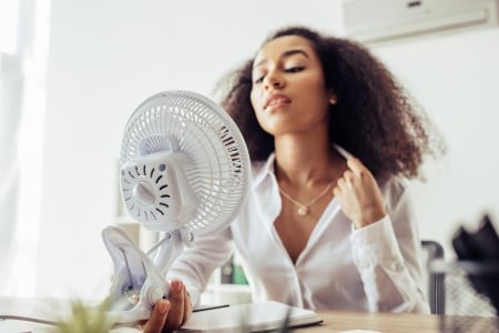 Jeune femme tentant de se rafraichir l'été avec un ventilateur de table