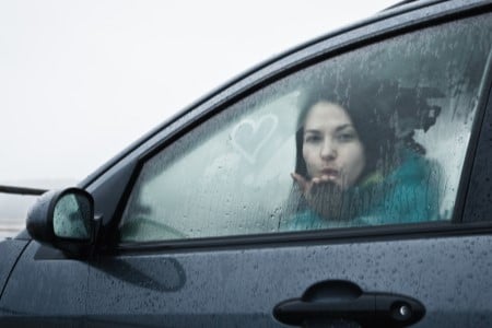 Jeune femme soufflant un baiser depuis sa voiture pleine de buée